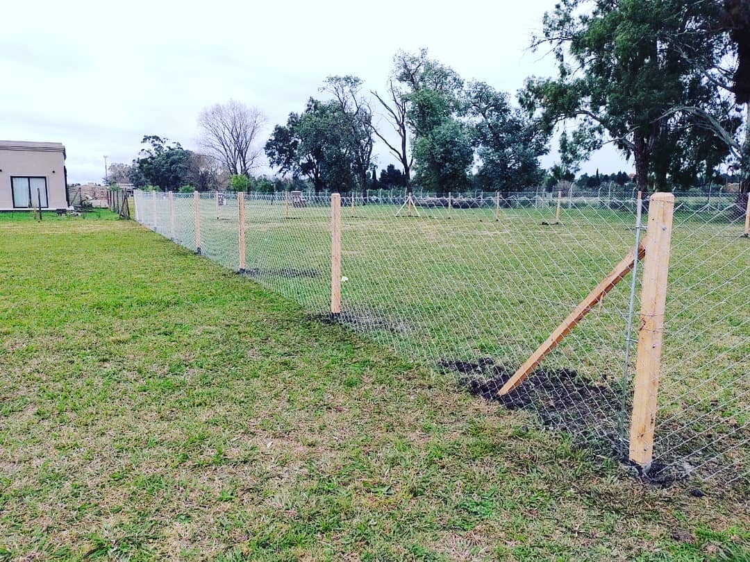 Alambrado perimetral con postes de madera y tejido romboidal a lo largo de un lote con césped.