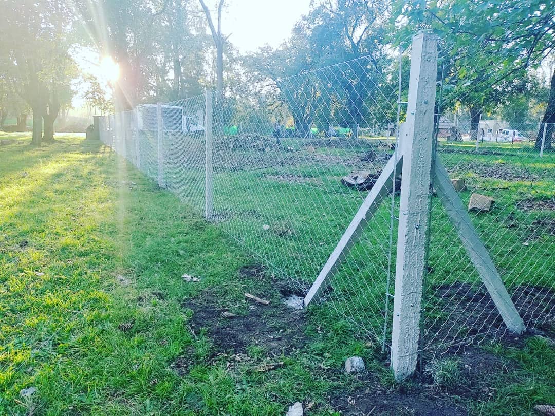 Cerco perimetral de tejido romboidal con postes de hormigón, recién instalado en un lote parquizado.
