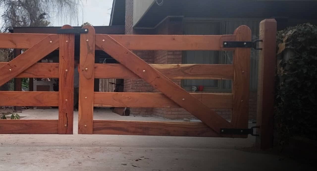 Portón doble de madera con cruz de refuerzo en la entrada de una casa.